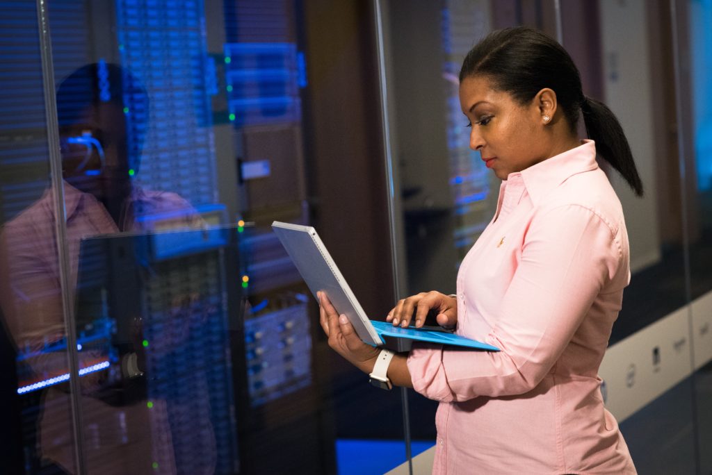 Uma mulher negra atuando coo DPO  com um notebook na mão analisando dados em frente a um data center